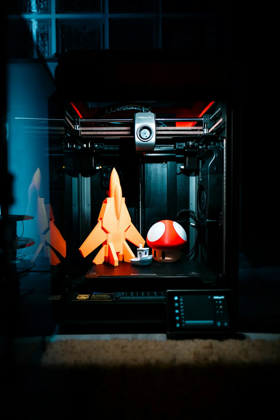Gotovi 3D printani modeli — narančasti maketni objekti ispred 3D printera